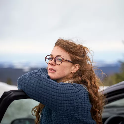 Woman with glasses leans over car door | Femme avec des lunettes se penchant sur la portière de la voiture.