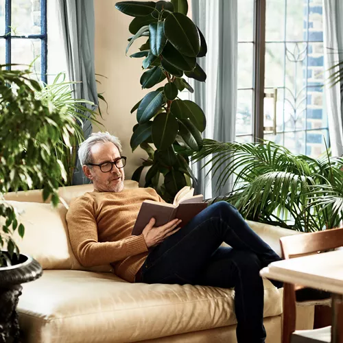 Older man with reading glasses reading book on couch