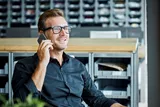 Szőke férfi fekete keretes szemüveggel telefonál