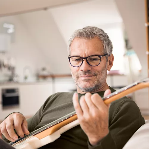 Un uomo anziano indossa lenti progressive HOYA mentre suona la chitarra