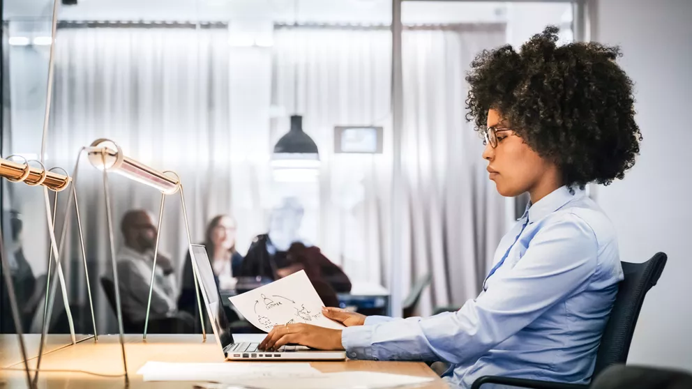 Woman with glasses working on a laptop behind a desk