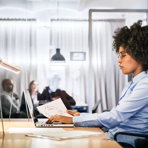 Woman with glasses working on a laptop behind a desk