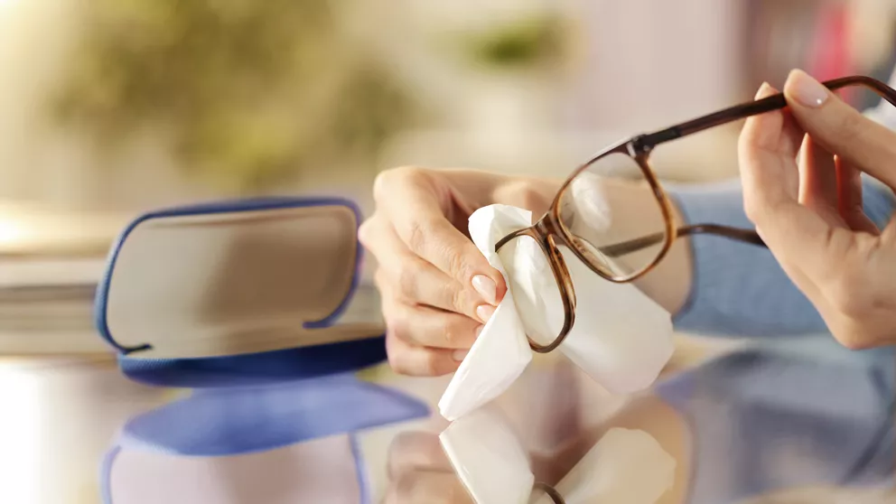 Person cleaning anti-bacterial lenses with white cloth