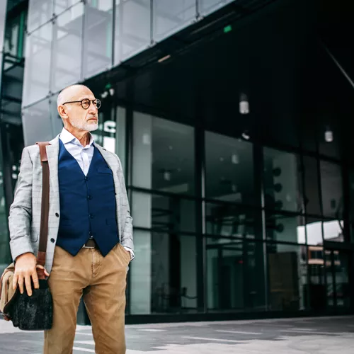 Older man wearing glasses standing in front of building