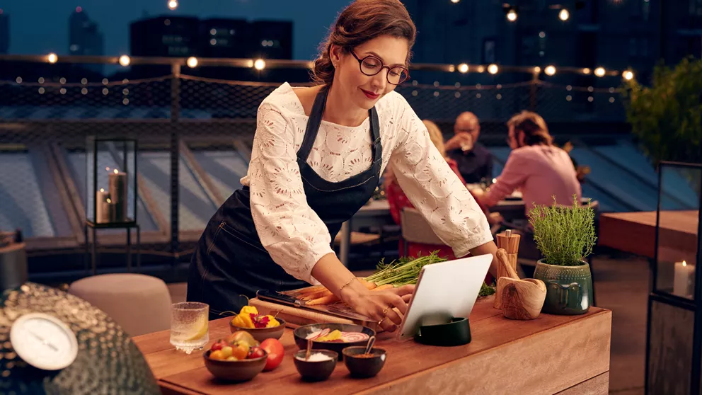 Chef con gli occhiali guarda il tablet mentre cucina