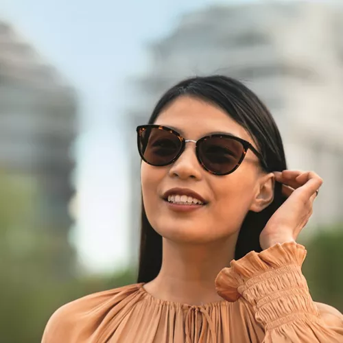 Smiling woman wearing HOYA polarized sunglasses and an orange top