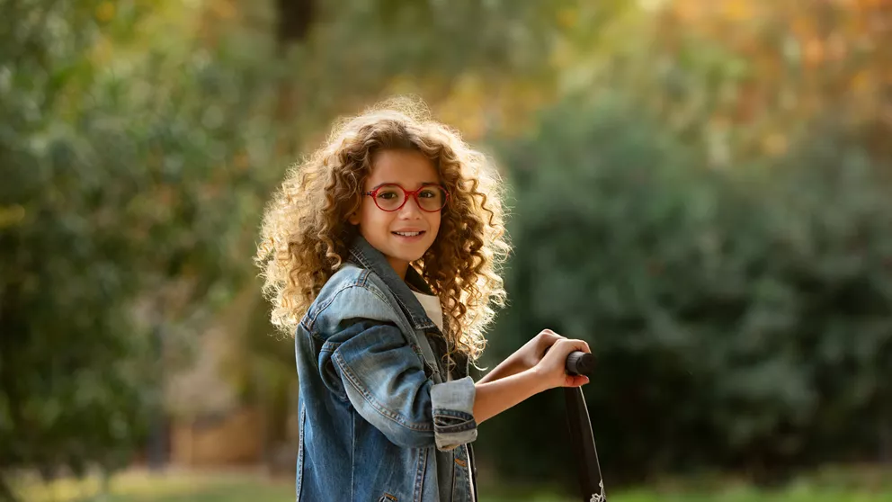 Girl with red glasses playing outside with a scooter