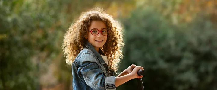 Girl with red glasses playing outside with a scooter