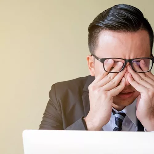 Uomo con gli occhiali che si strofina gli occhi mentre lavora al computer portatile