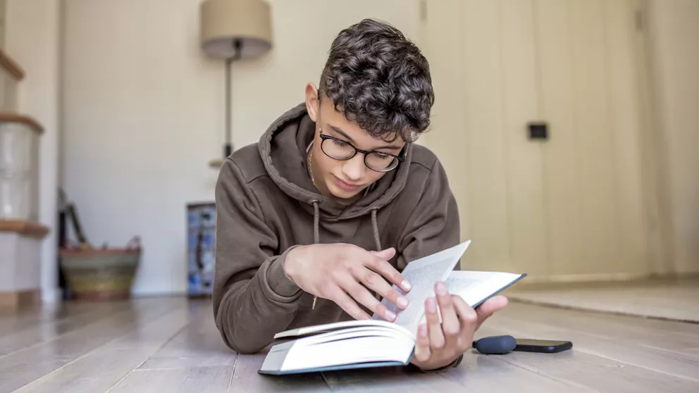 Boy with curly hair and glasses holding and reading a book