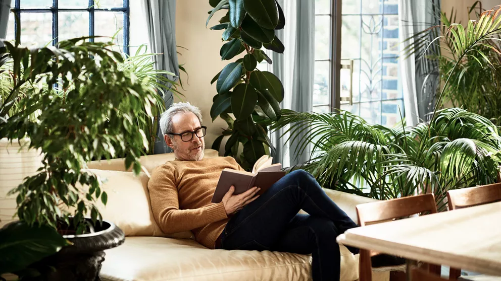 Older man with black framed glasses reading a book on the couch