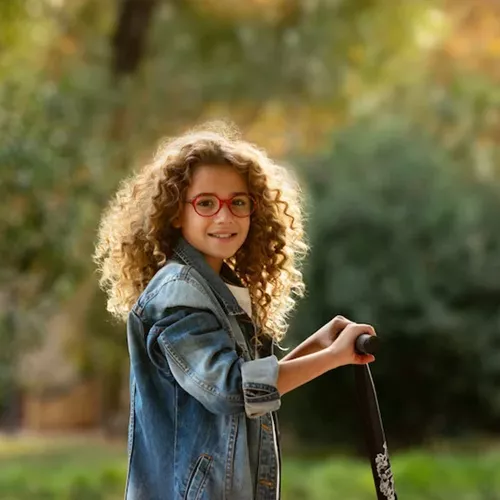 Girl with curly hair and red glasses playing outdoors