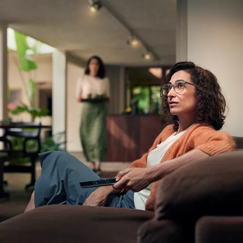 Woman with curly brown hair and glasses sits on a couch