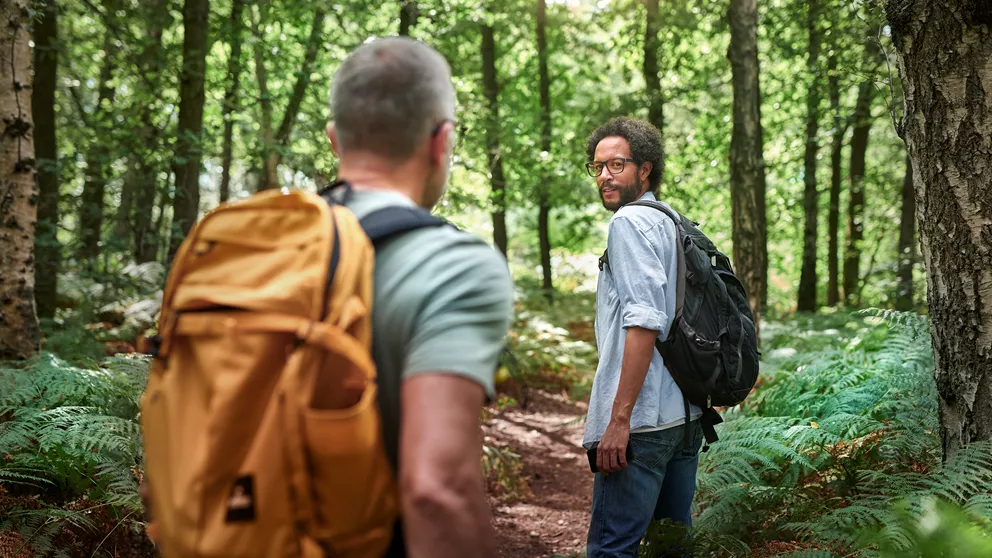 Two men wearing backpacks hiking in a forest