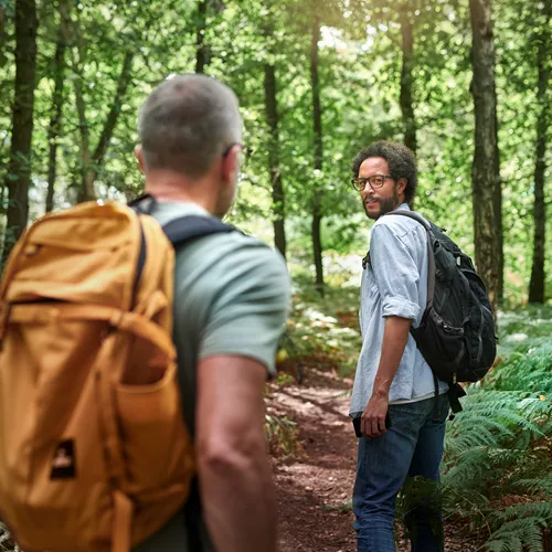 Two men wearing backpacks hiking in a forest