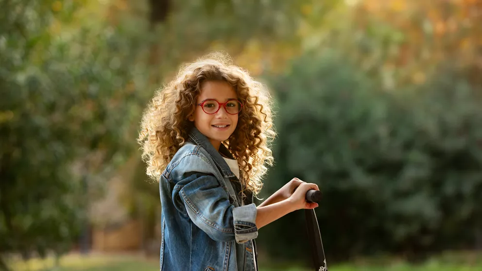 Meisje met krullend haar speelt buiten terwijl ze een HOYA MiYOSMART-bril draagt