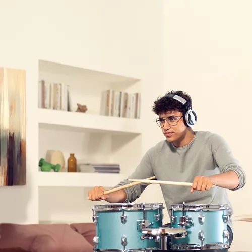 Man with headphones and glasses playing a blue drumkit in a living room