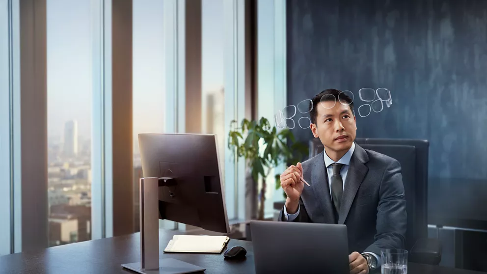 Man in suit behind desk, wearing HOYA MySelf Profile glasses with a halo of lenses around his head