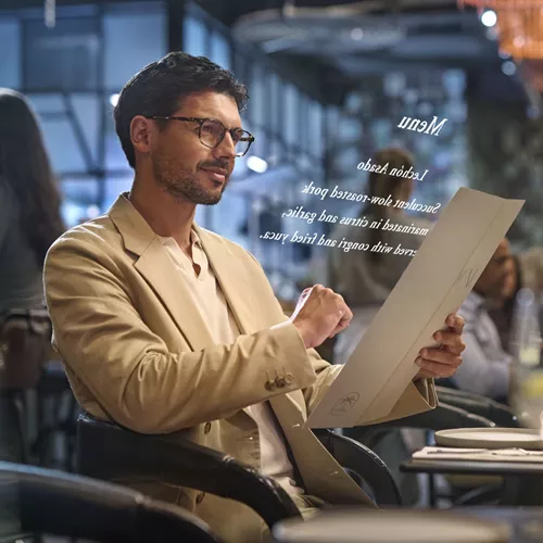 Bej takım elbiseli adam, restoran menüsünü okumak için HOYA VisuPro gözlük takıyor