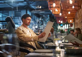 Mann im beigen Anzug hat Schwierigkeiten, die Speisekarte eines Restaurants zu lesen
