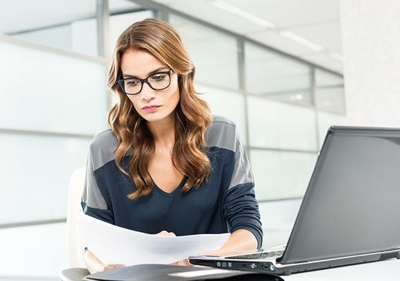 Female sat at a desk wearing a pair of Hoya Vision eyeglass lenses reading from a page