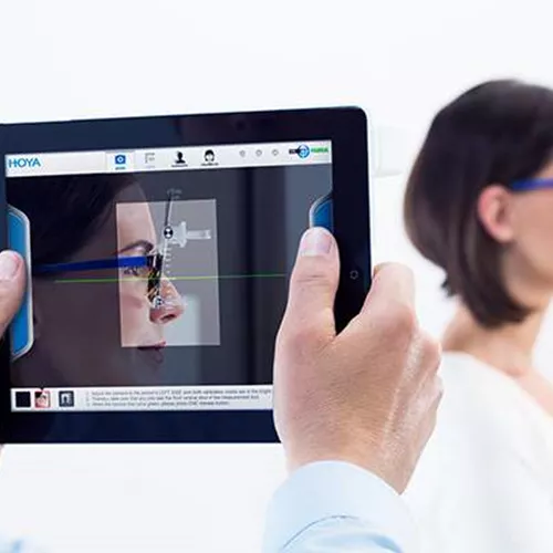 Male optician using a tablet to measure a pair of eyeglasses with Hoya Vision lenses on a females face