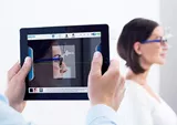 Male optician using a tablet to measure a pair of eyeglasses with Hoya Vision lenses on a females face