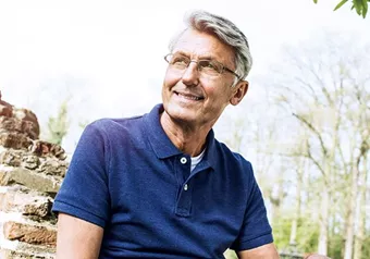 Older male wearing eyeglasses with Hoya Vision lenses sitting on a brick wall 