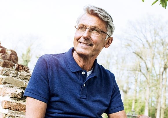 Older male wearing eyeglasses with Hoya Vision lenses sitting on a brick wall