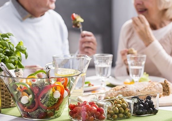 Range of healthy food on a table with an elderly couple behind