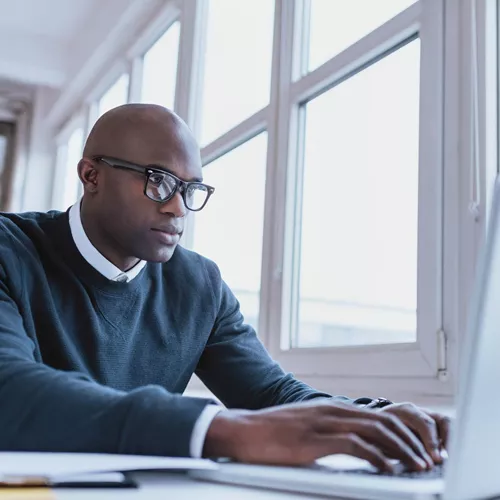 Male working on a laptop indoors wearing eyeglasses with Hoya Vision signle vision lenses