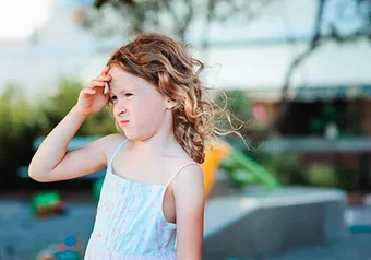 Young girl outdoors shading her eyes from the sun