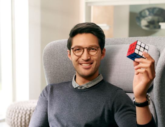 Male wearing eye glasses with Hoya Vision lenses holding a rubik's cube