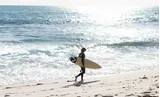 Male surfer walking along a beach carrying a surfboard 