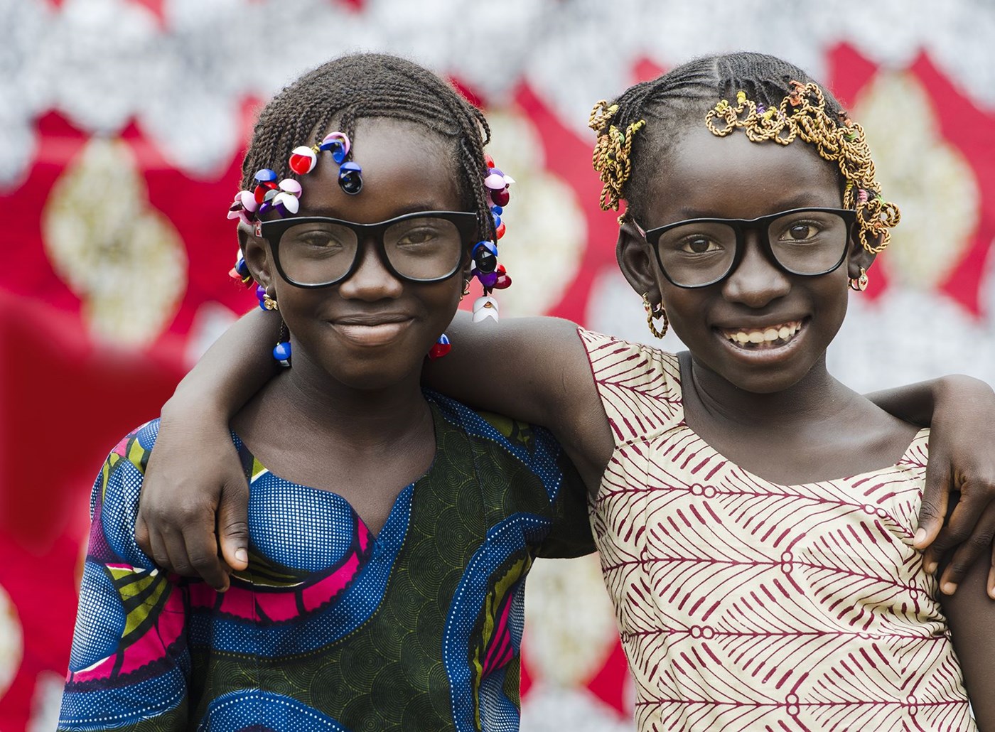Two girls with braids embracing each other wearing eye glasses with Hoya Vision lenses