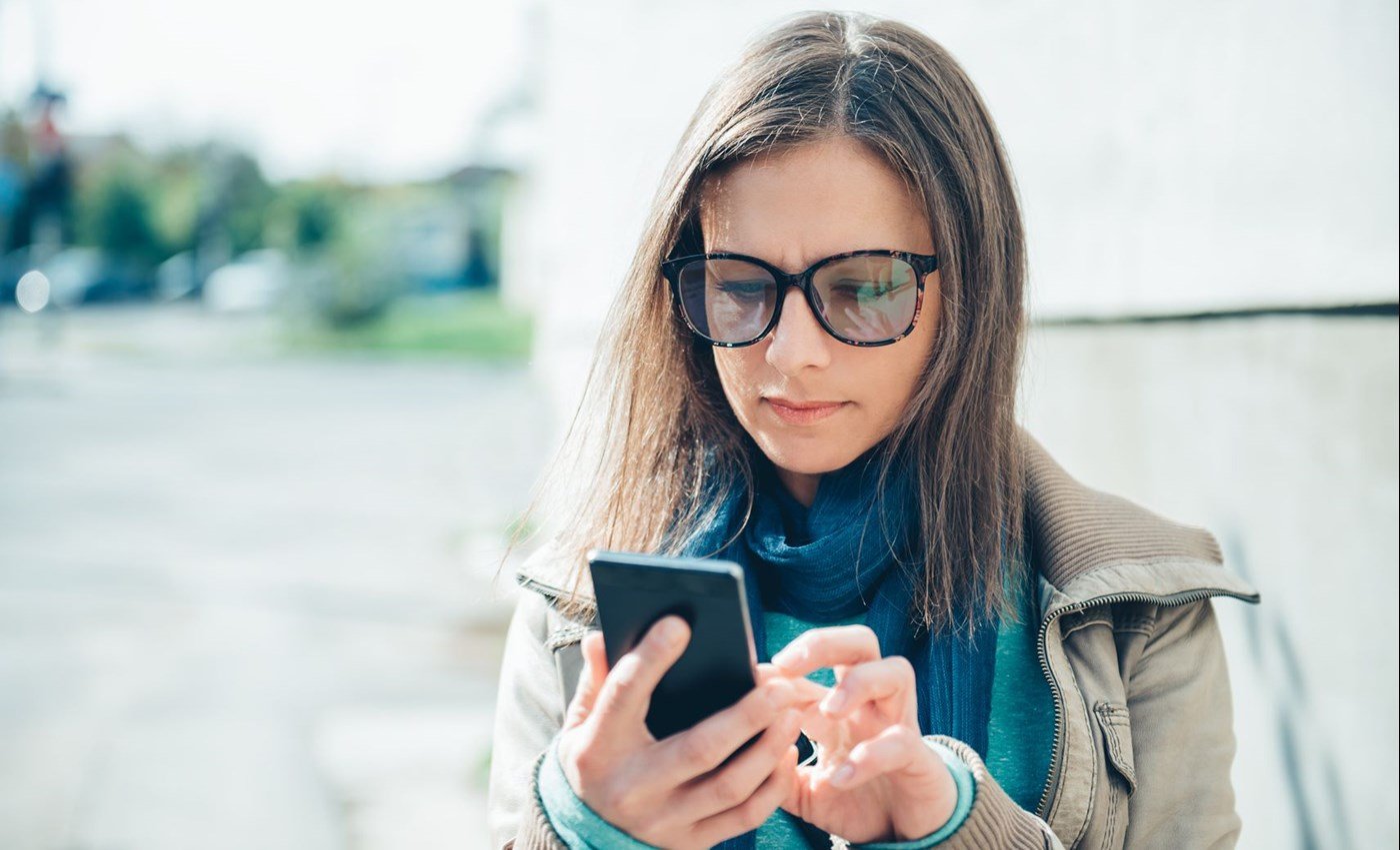 Woman scrolling on her mobile phone wearing eyeglasses with Hoya Vision photochromic lenses