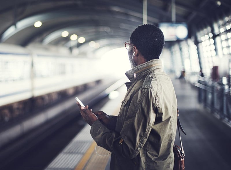 Male wearing eyeglasses holding mobile phone at a train station