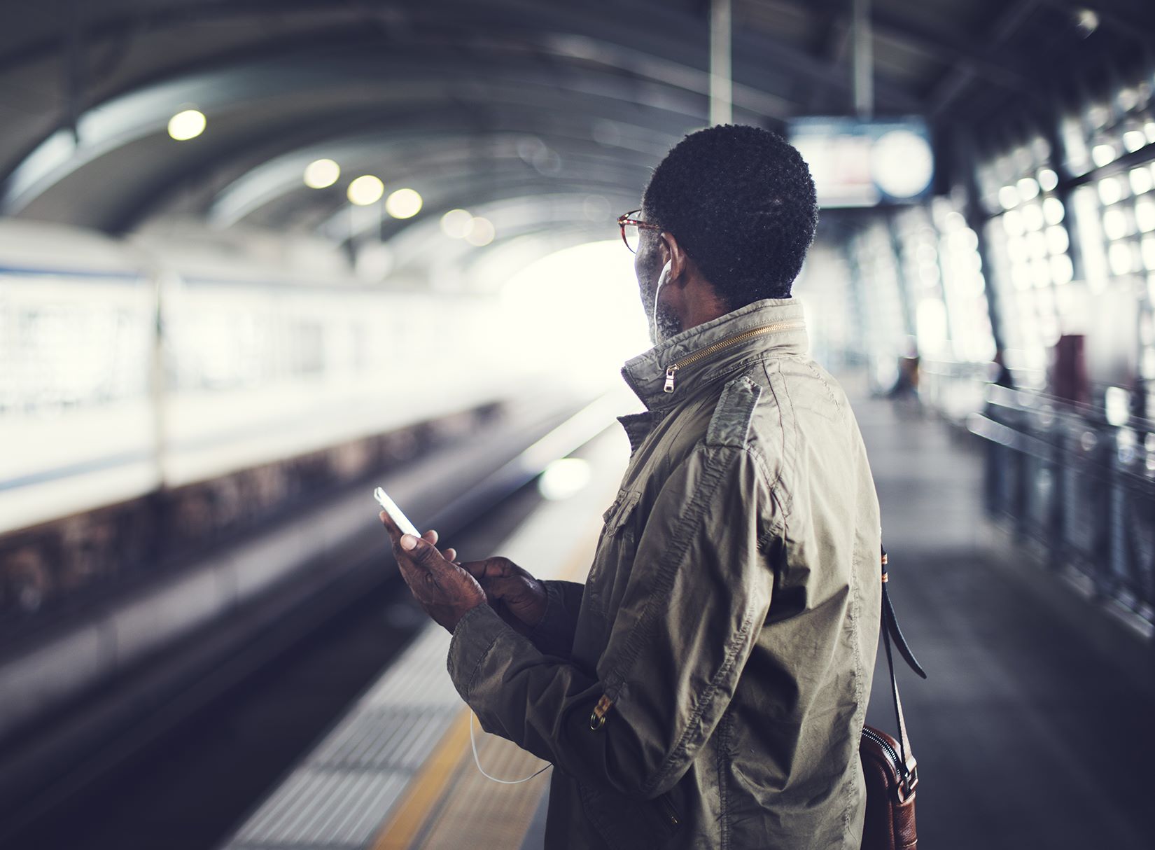 Male wearing eyeglasses holding mobile phone at a train station