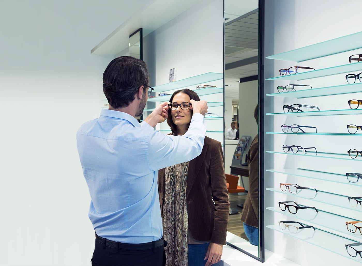 Male Hoya Vision optician placing eyeglasses on a female