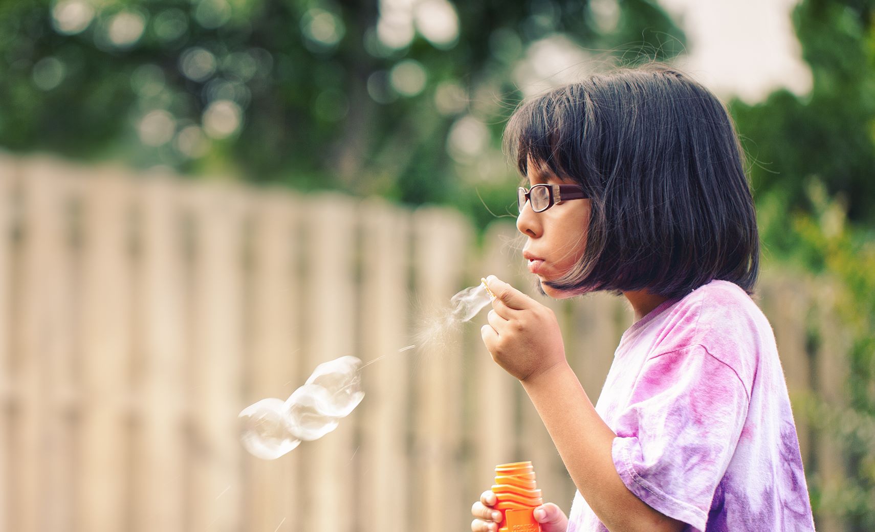 Young girl blowing bubbles wearing eyeglasses with Hoya Vision children's lenses