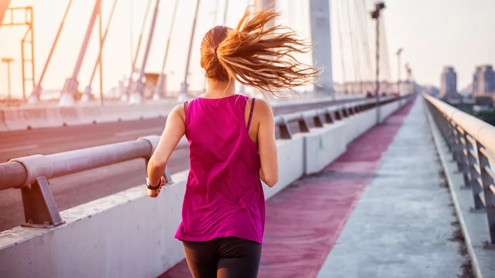 Woman in pink top running along a bridge