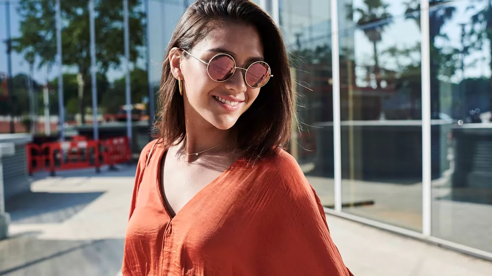 Woman in red top wearing round sunglasses with Hoya Vision polarized tinted lenses