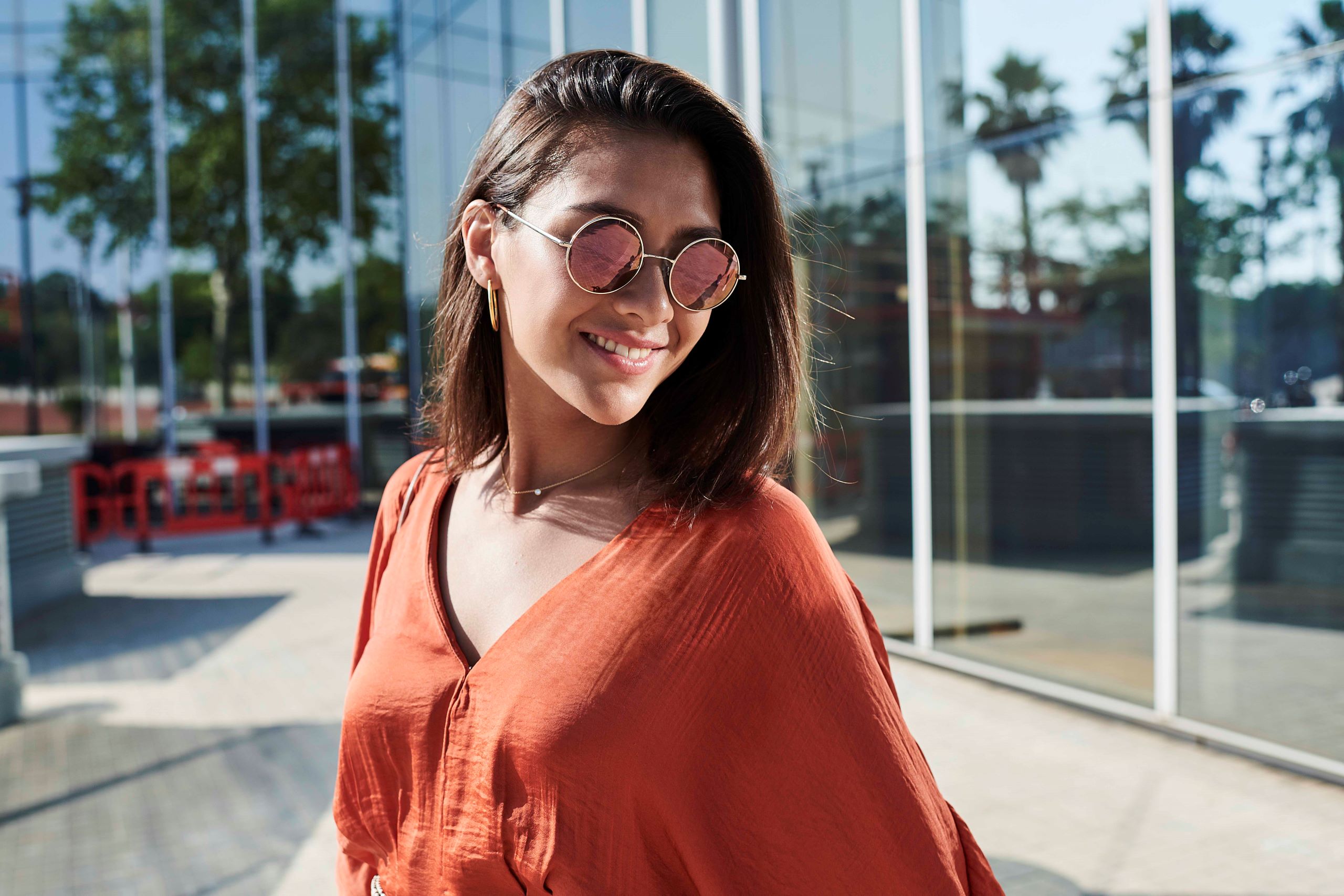 Woman in red top wearing round sunglasses with Hoya Vision polarized tinted lenses