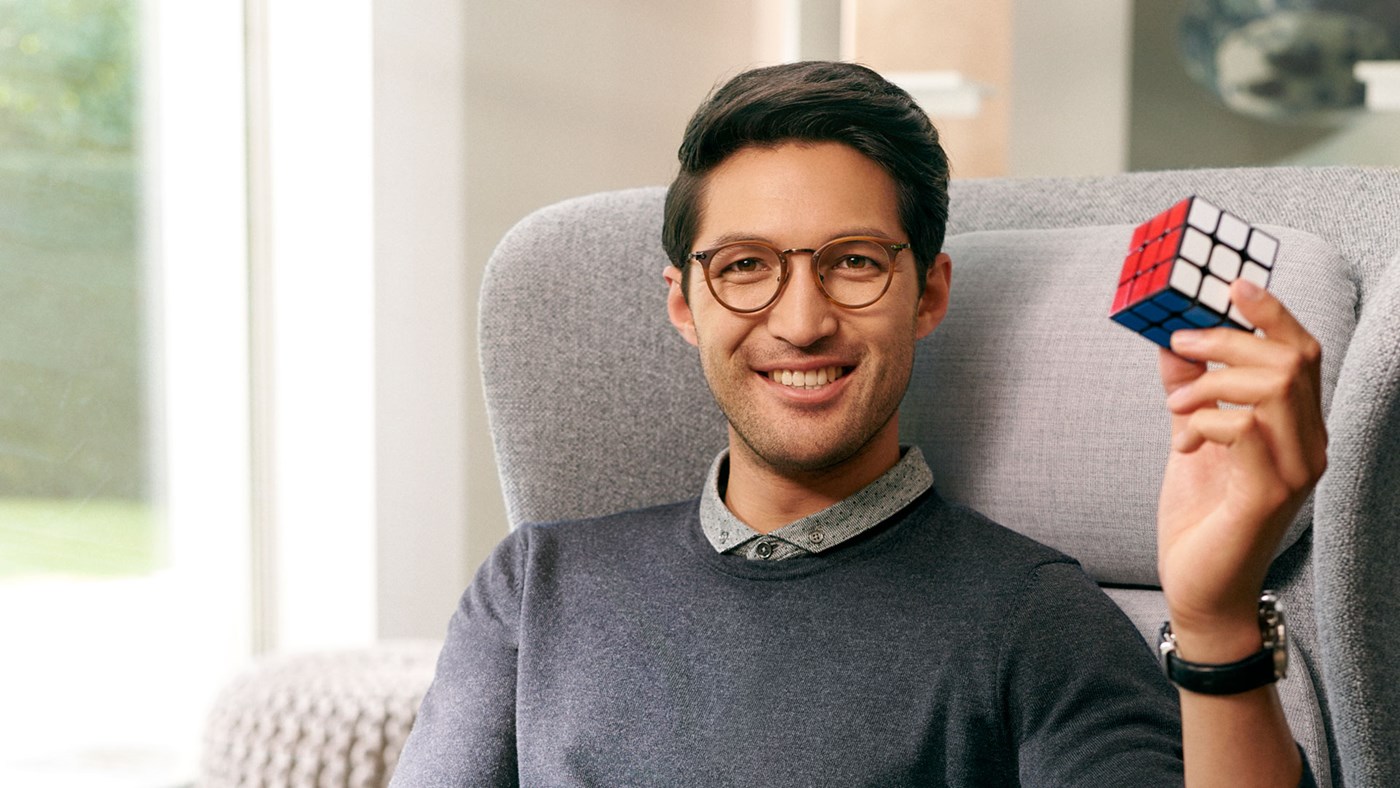 Male wearing eyeglasses with Hoya Vision lenses holding a Rubik's cube