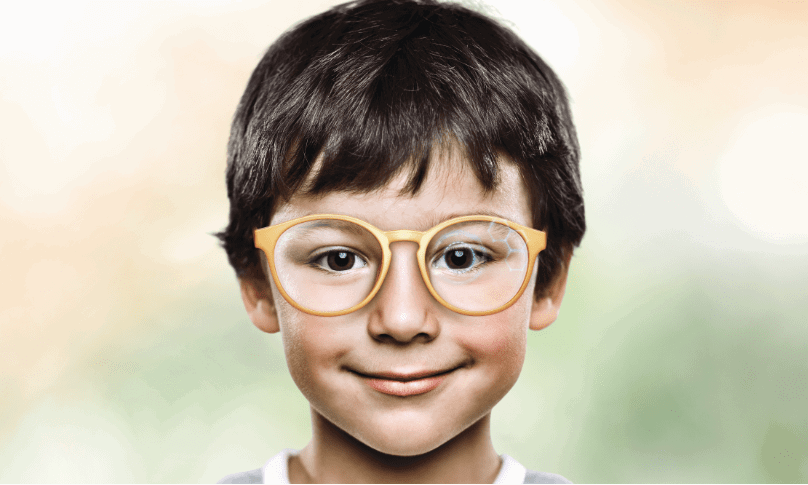 Young boy wearing eyeglasses staring and smiling at camera