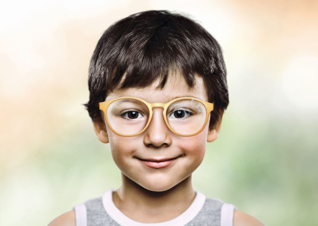Young boy wearing orange eyeglass frames with myosmart lenses smiling at camera