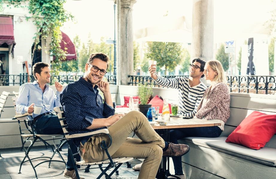 Male sat at table with three others wearing eyeglasses looking at camera smiling