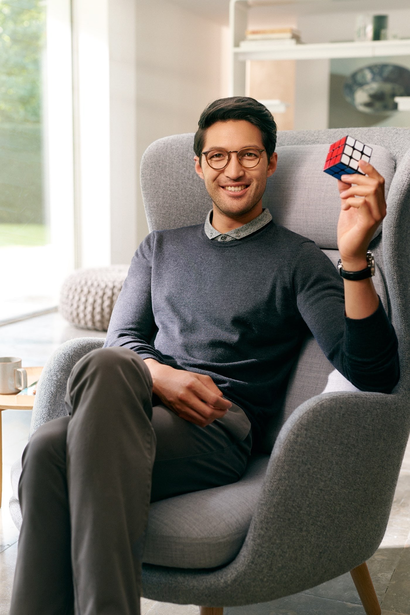 Male sat on chair wearing eyeglasses holding Rubik's cube