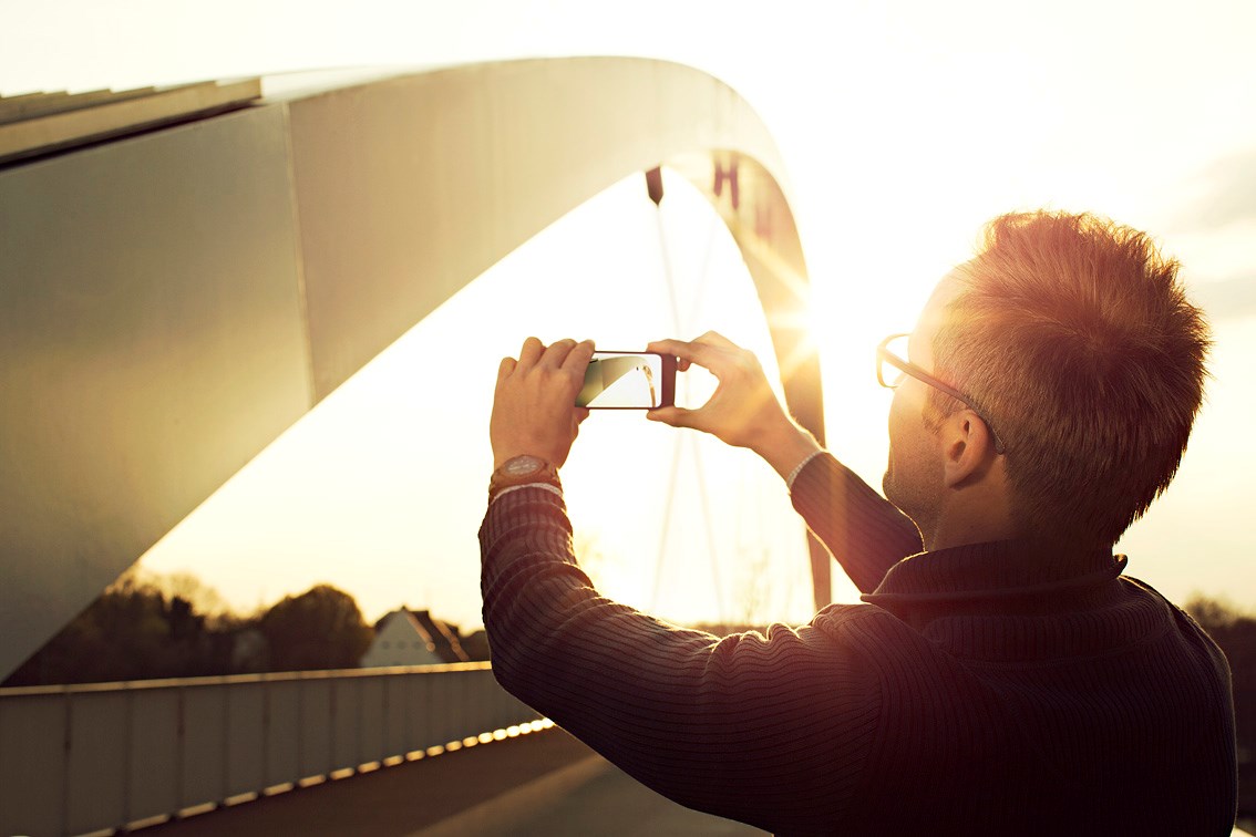 Male wearing eyeglasses taking image of bridge on smartphone