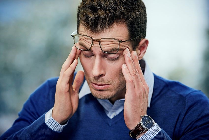 Male rubbing temples with glasses on top of head